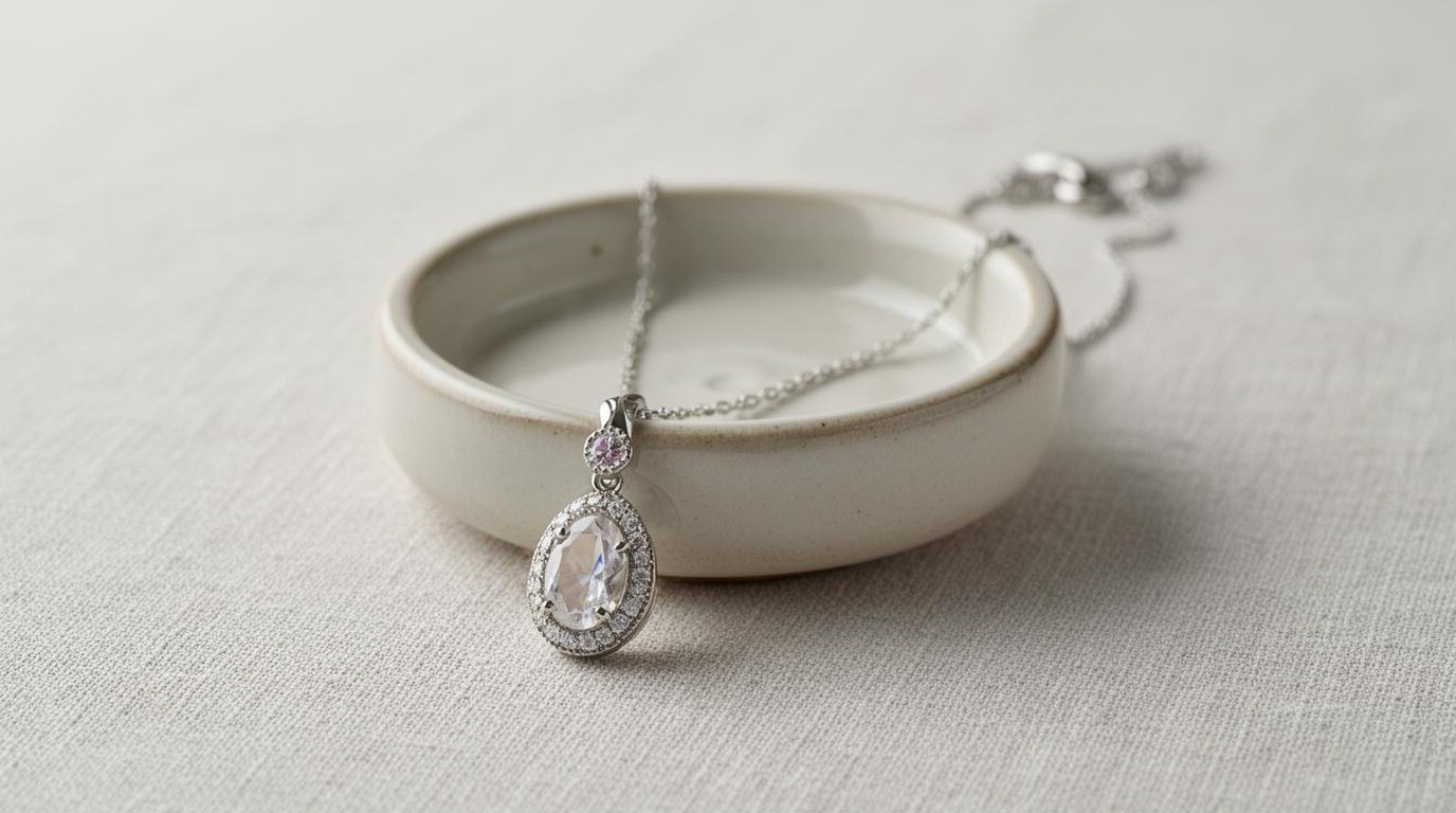 A delicate gold pendant necklace draped over a small ceramic dish
